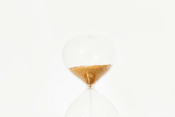 A brass hourglass with sand mid-flow on a dark surface, representing the ninety day sequence for a first AI program