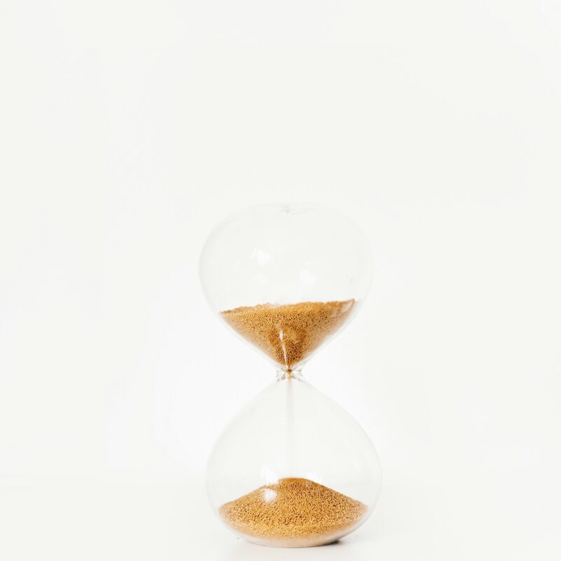 A brass hourglass with sand mid-flow on a dark surface, representing the ninety day sequence for a first AI program