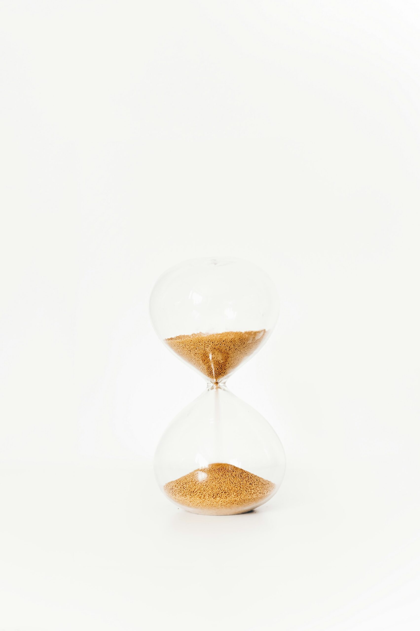 A brass hourglass with sand mid-flow on a dark surface, representing the ninety day sequence for a first AI program