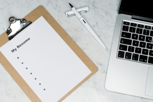 Resume on a clipboard beside a laptop, illustrating AI in hiring