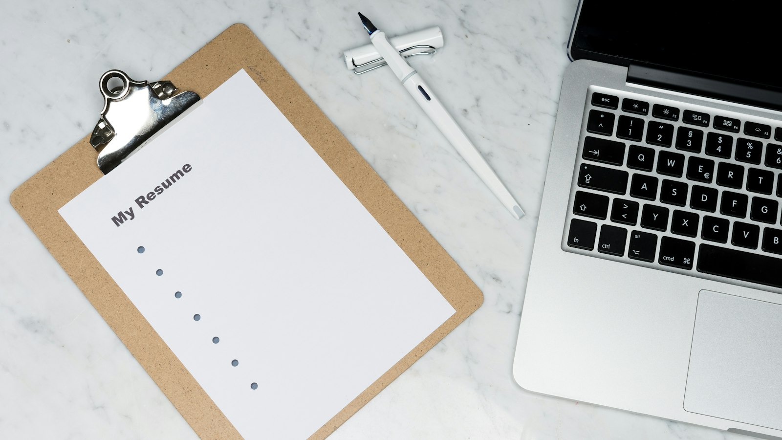 Resume on a clipboard beside a laptop, illustrating AI in hiring