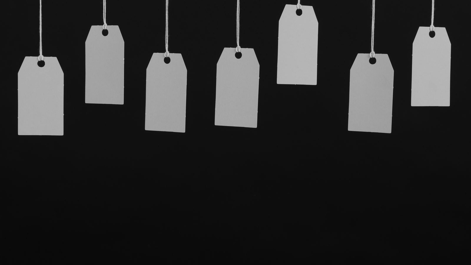 A row of blank price tags hanging on strings against a dark background