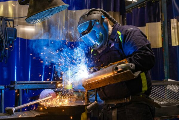 Welder cutting metal in a shop with sparks flying, illustrating custom AI vs off-the-shelf
