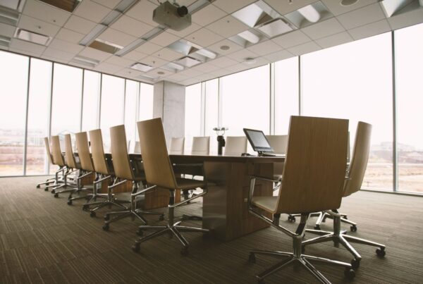 An empty boardroom table and chairs beside tall windows