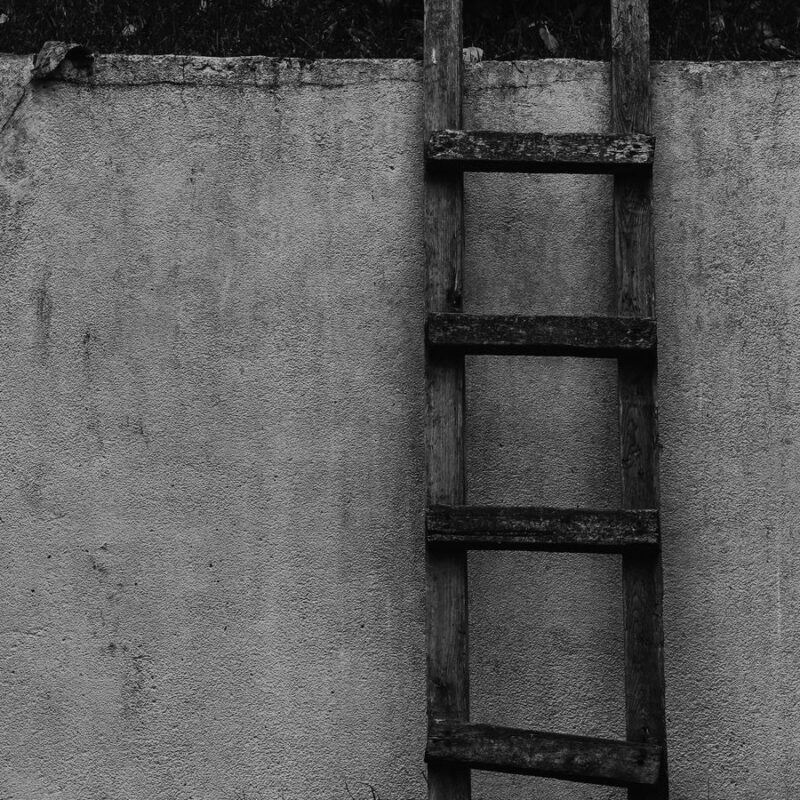 A wooden ladder leaning against a plain wall, every rung in view
