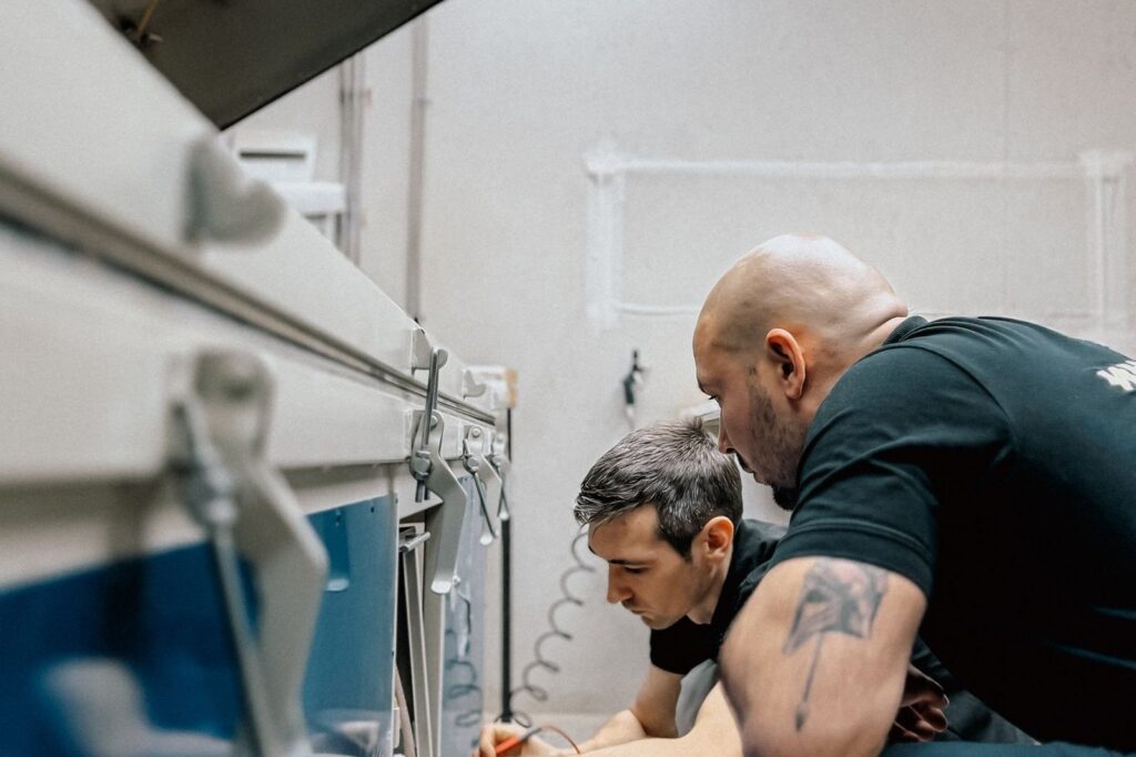 An experienced technician guiding a younger colleague at an industrial machine