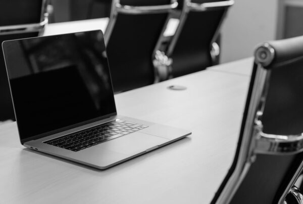 An open laptop on the far side of a meeting table, with chairs on both sides