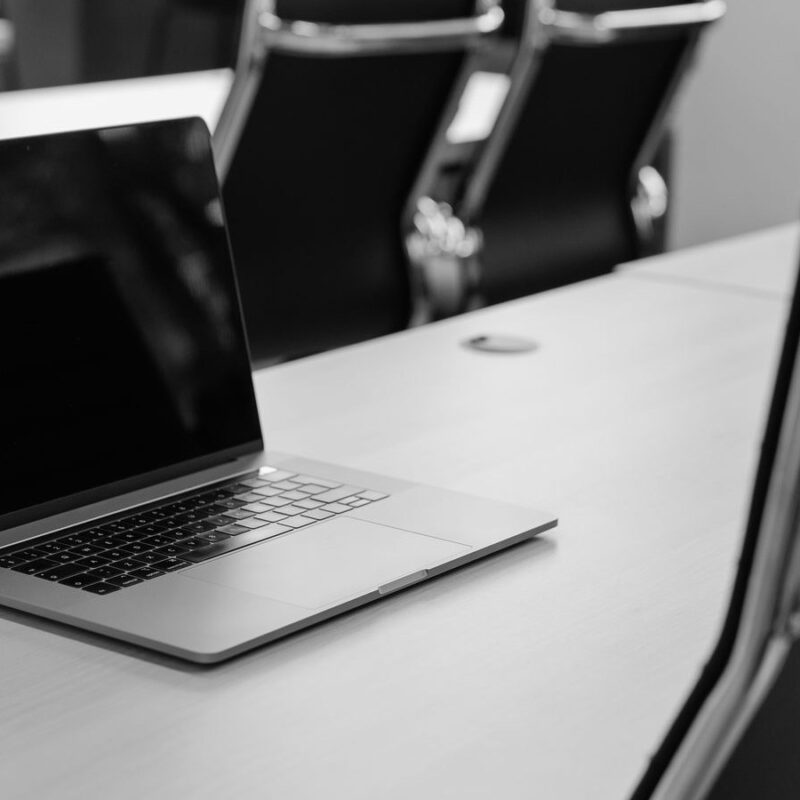 An open laptop on the far side of a meeting table, with chairs on both sides