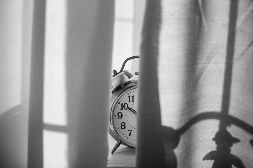 Black and white photo of a vintage alarm clock standing behind a sheer curtain in low light