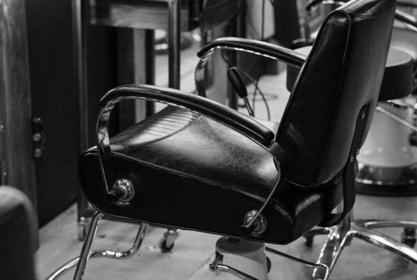A black leather barber chair standing empty in a salon.