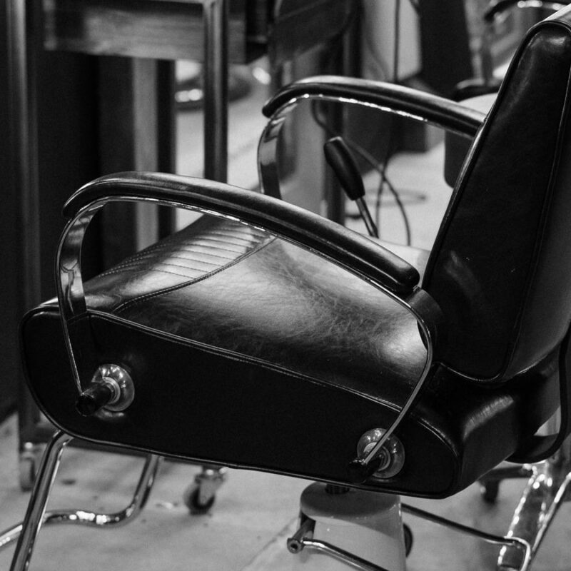 A black leather barber chair standing empty in a salon.