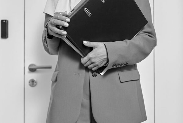 A person holding a thick black ring binder in front of an office door
