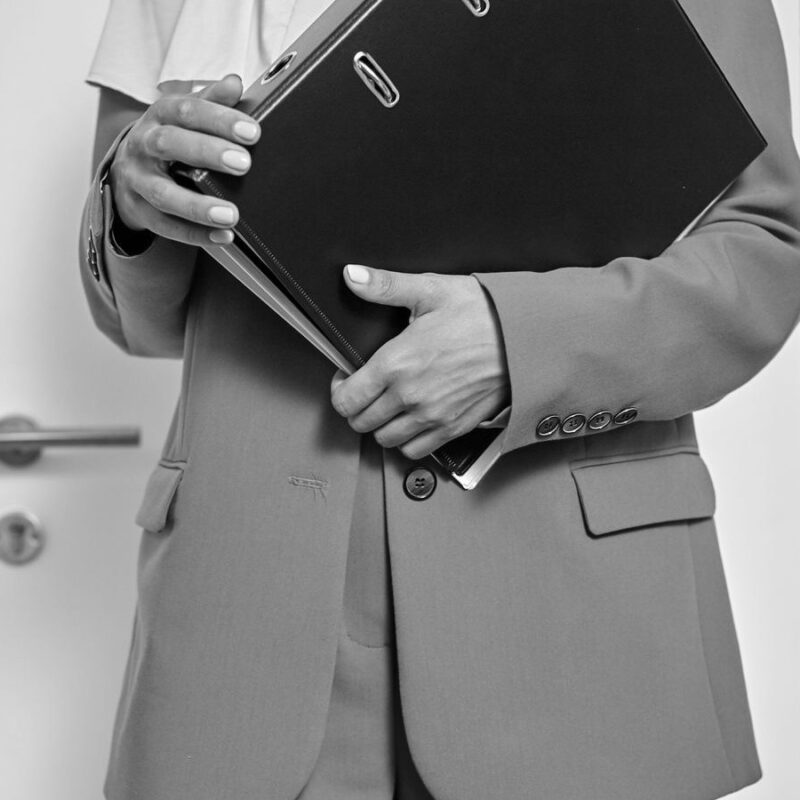 A person holding a thick black ring binder in front of an office door