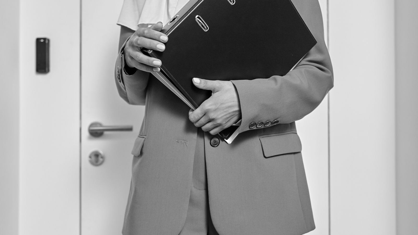 A person holding a thick black ring binder in front of an office door