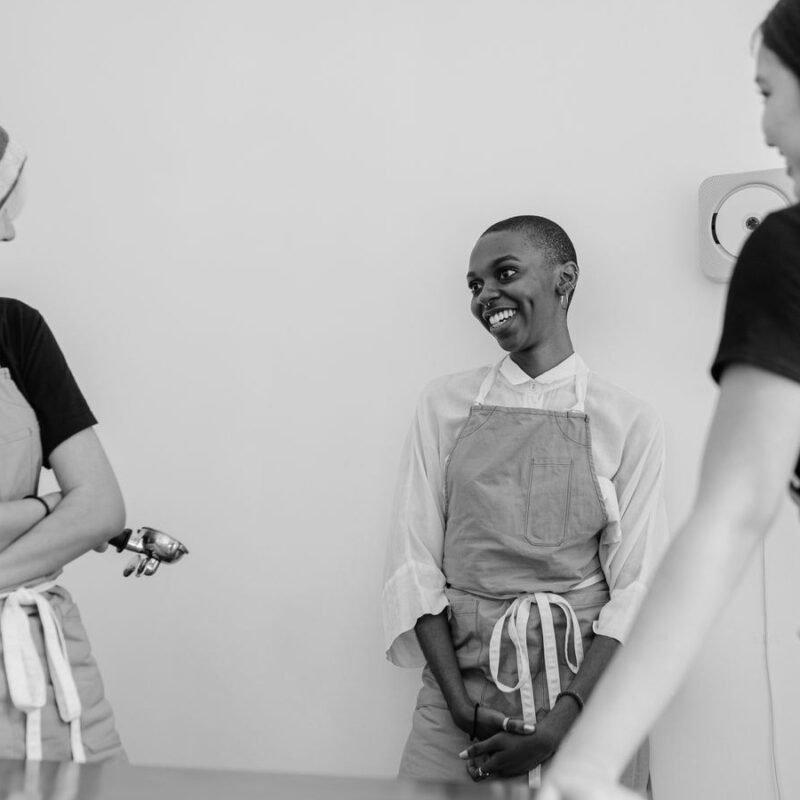 Three cafe staff in aprons talking at the counter