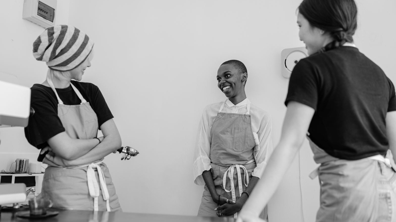 Three cafe staff in aprons talking at the counter