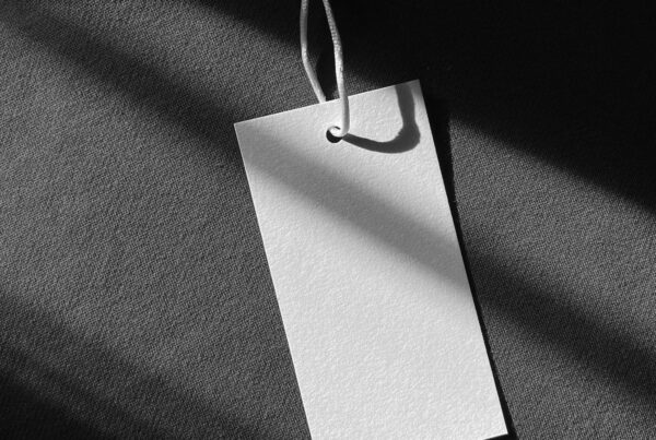 A blank clothing tag on a string resting against a dark garment in sunlight