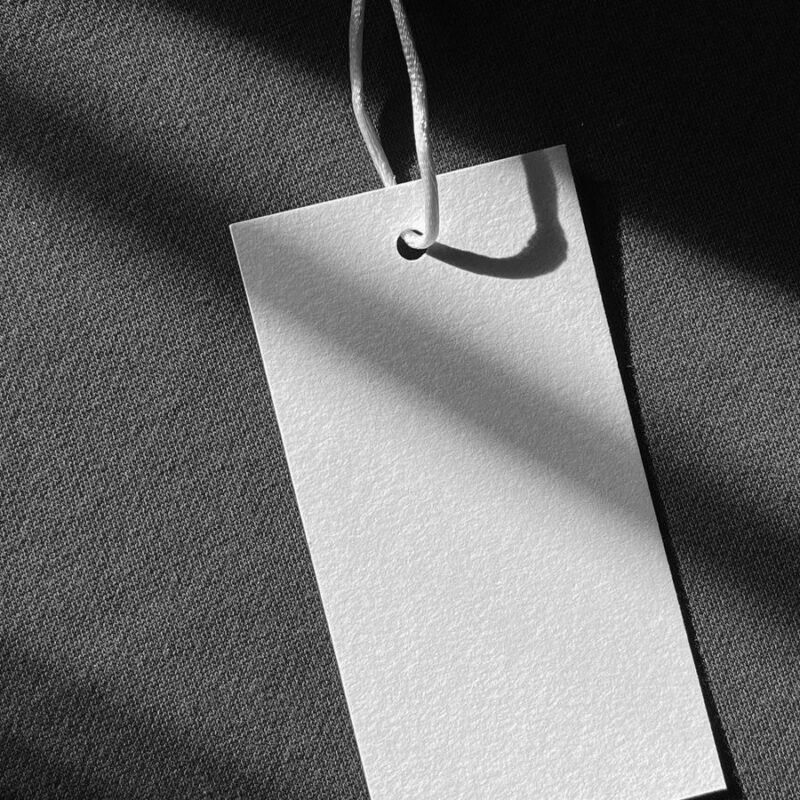 A blank clothing tag on a string resting against a dark garment in sunlight