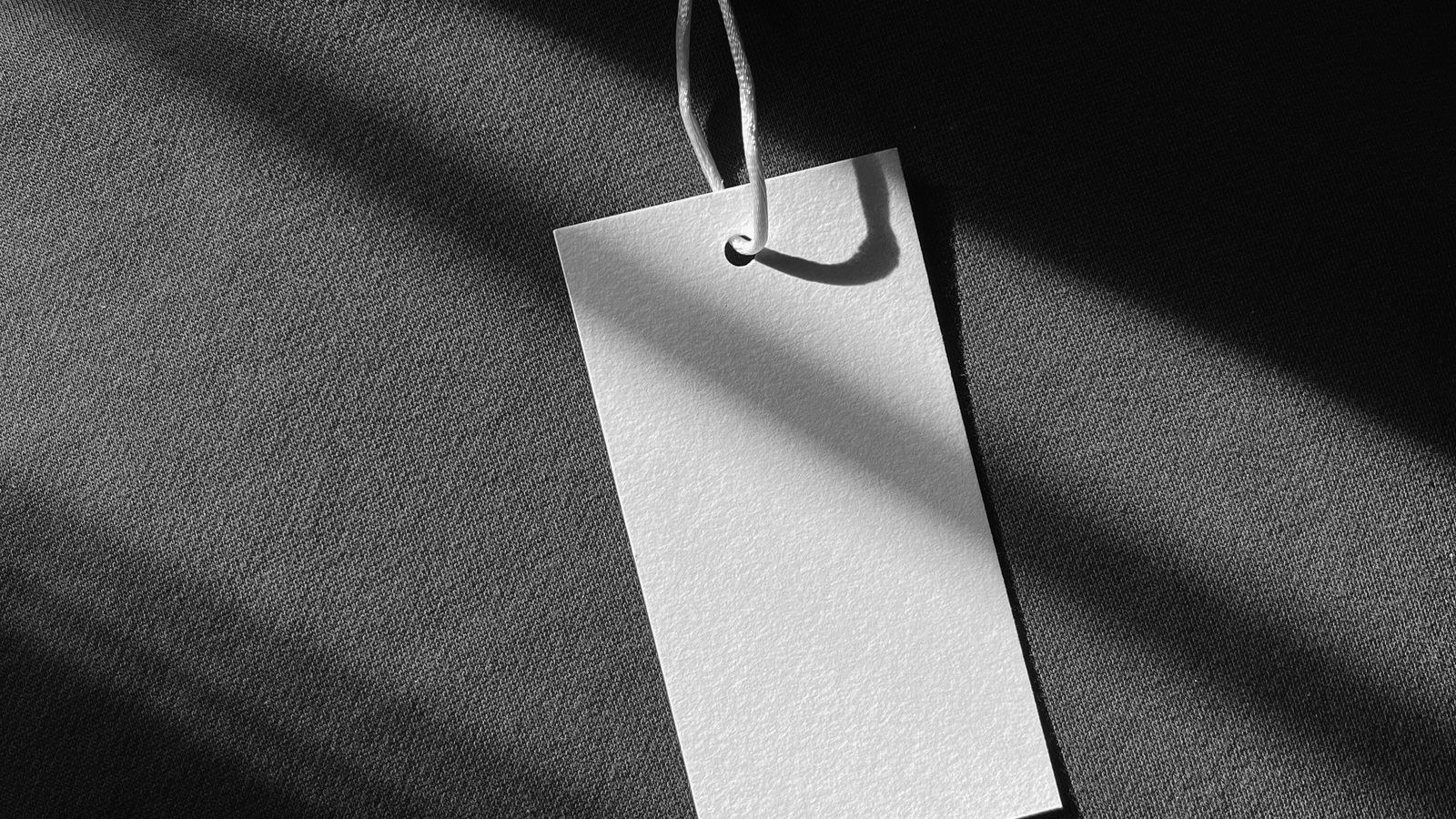 A blank clothing tag on a string resting against a dark garment in sunlight