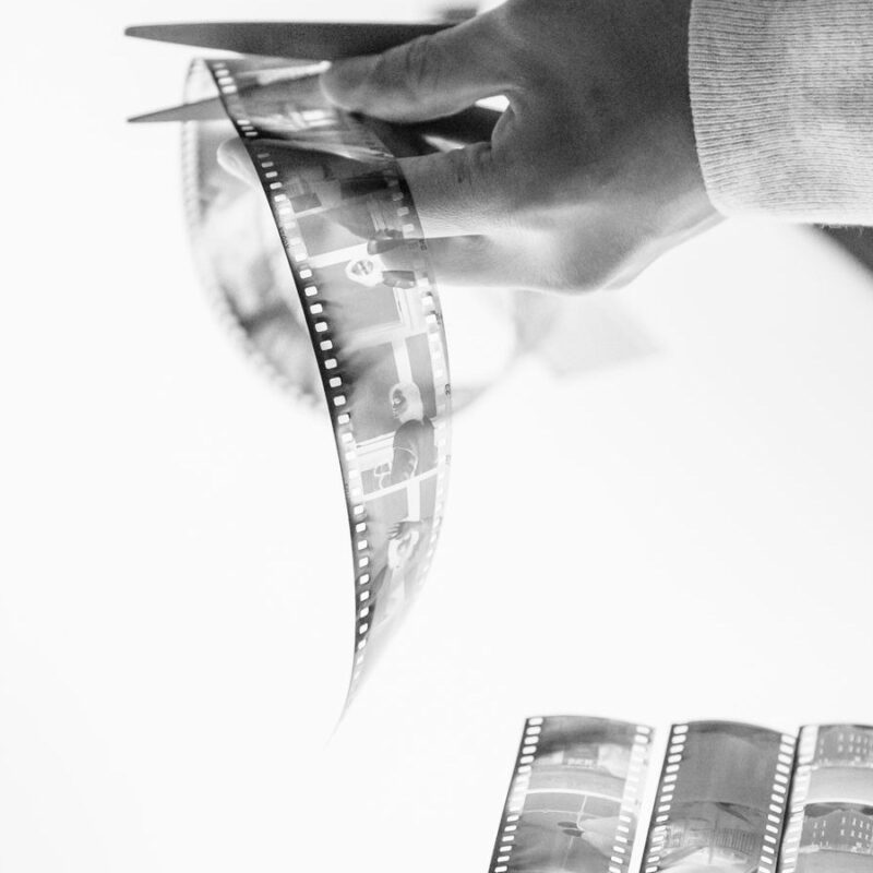 Hands cutting a strip of film with scissors over a light table