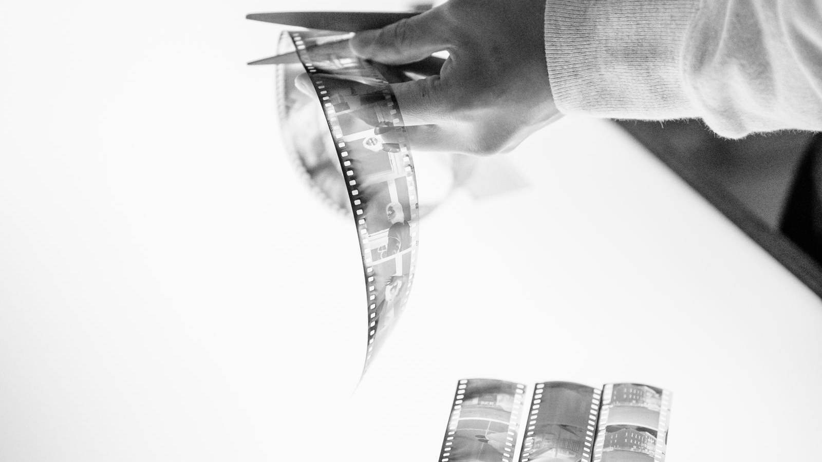 Hands cutting a strip of film with scissors over a light table