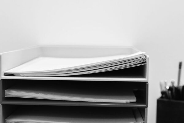 A stack of paper trays on an office desk, each tray holding folders and loose sheets