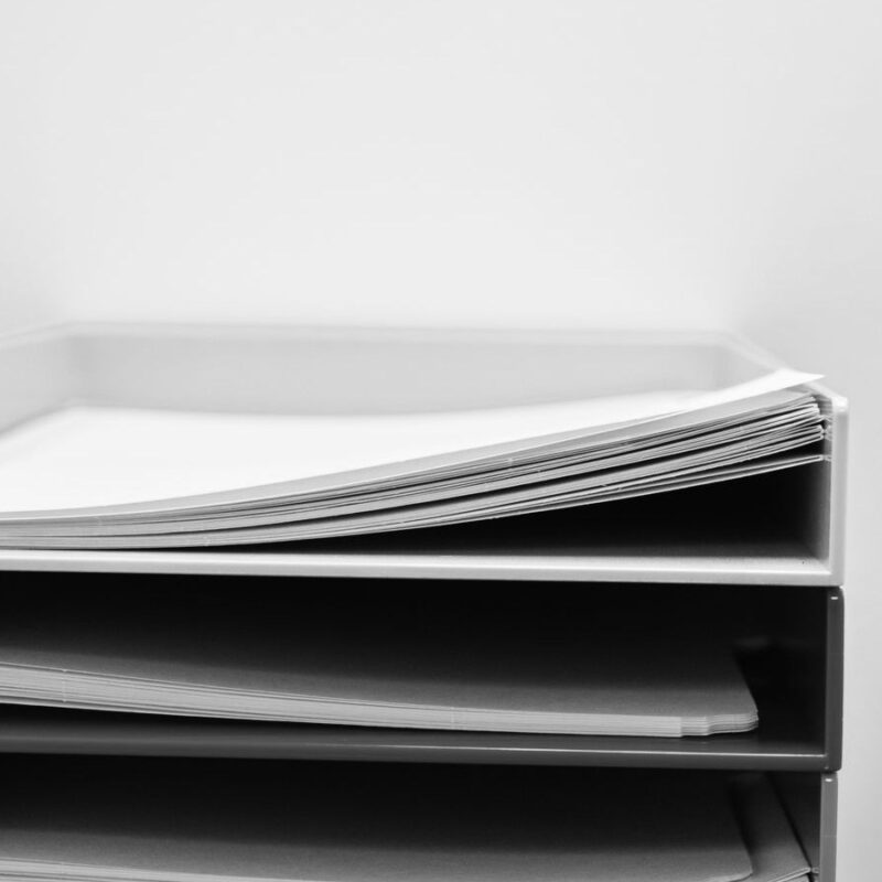 A stack of paper trays on an office desk, each tray holding folders and loose sheets