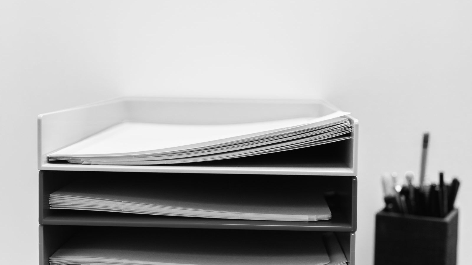 A stack of paper trays on an office desk, each tray holding folders and loose sheets