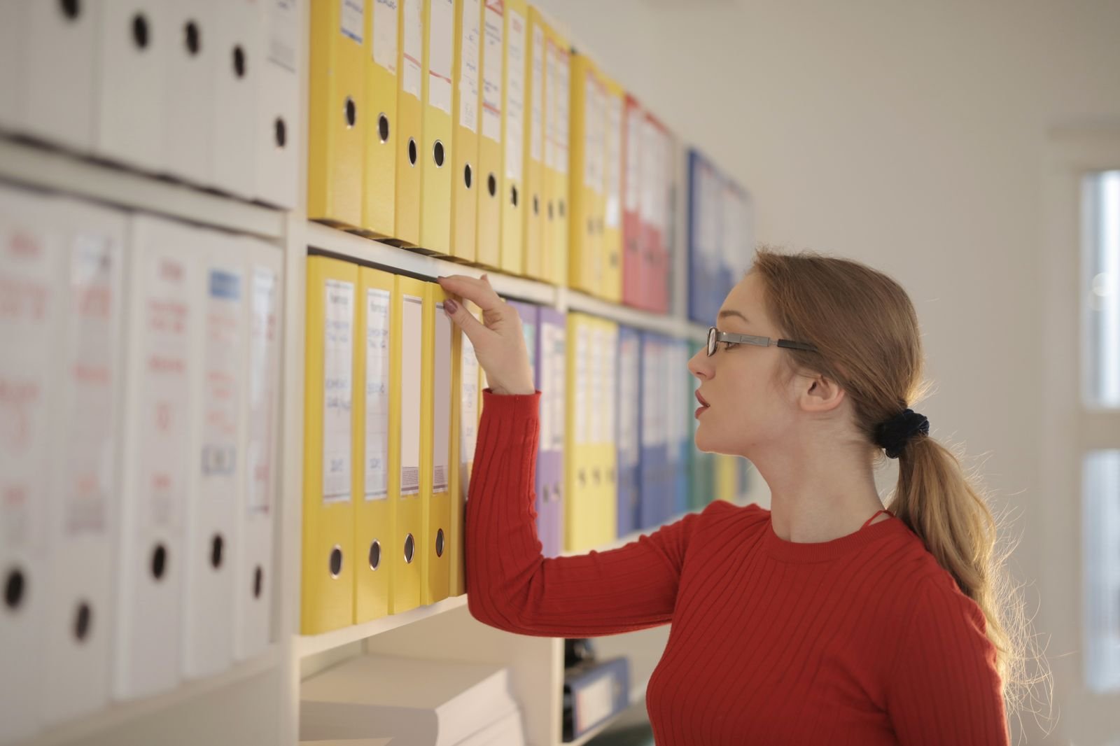 A hand reaching for a binder on a shelf of files
