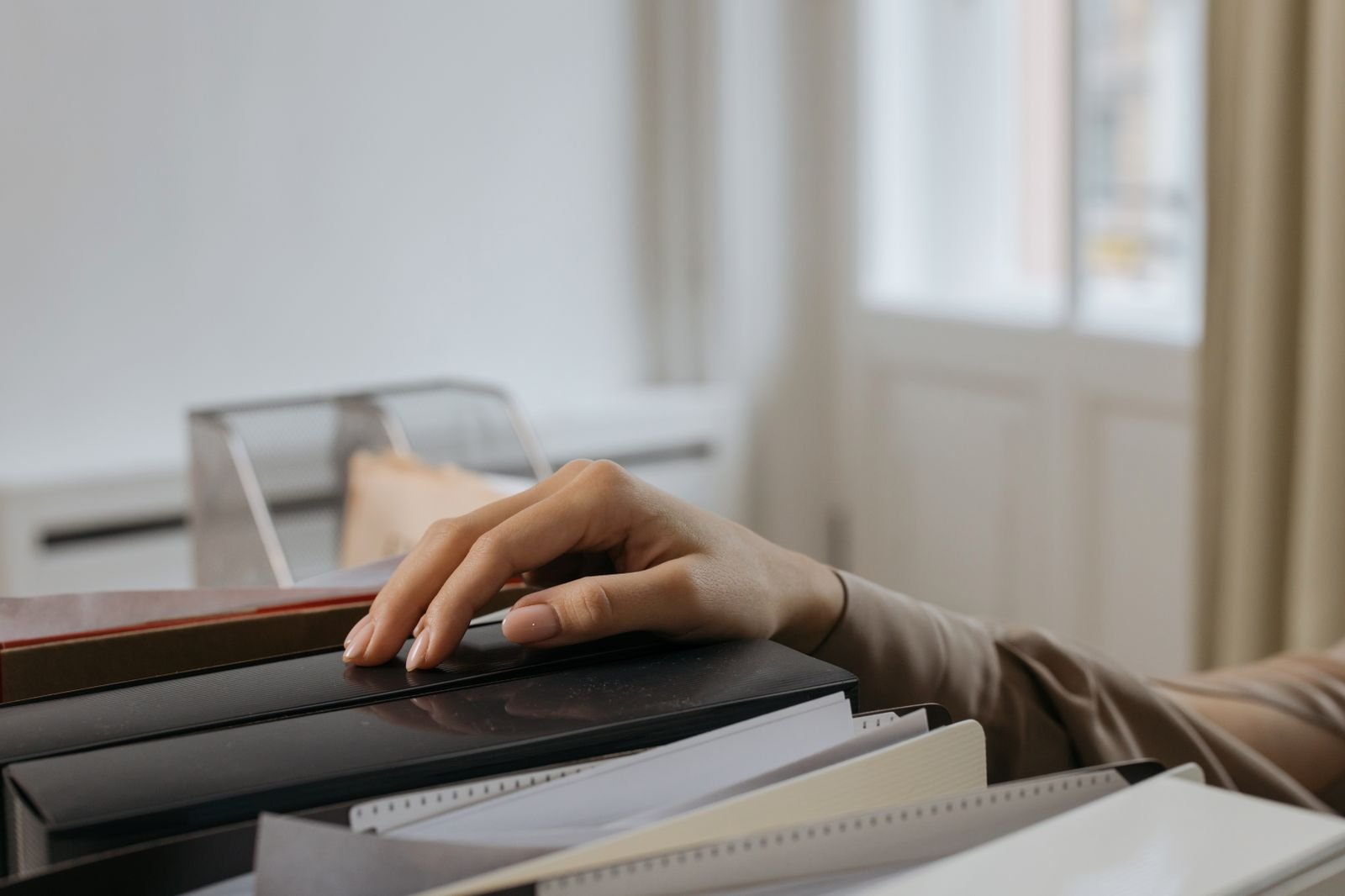 A hand on a row of file folders beside a desk tray