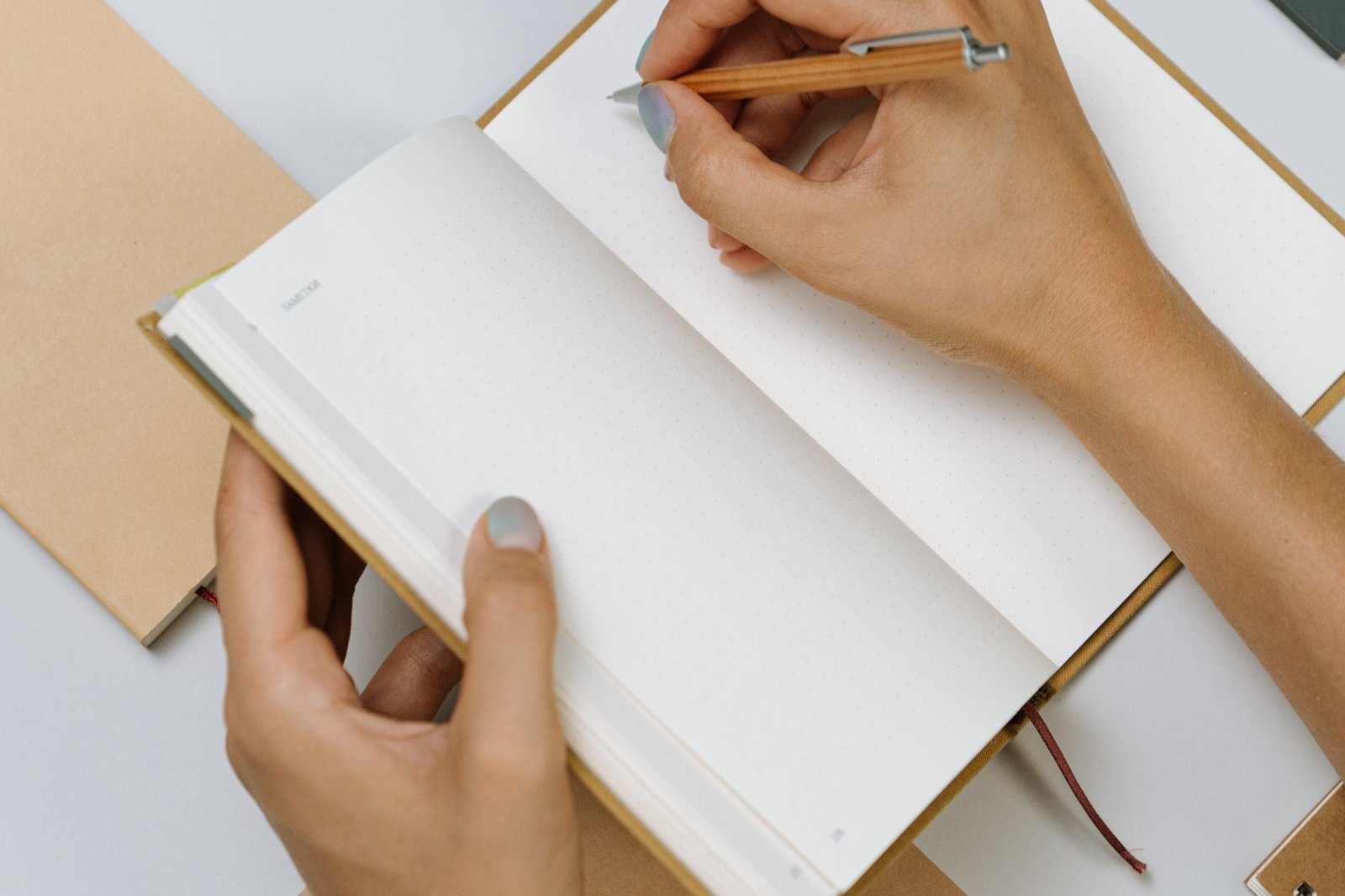 Hands writing in an open bound planner with a pen, seen from above
