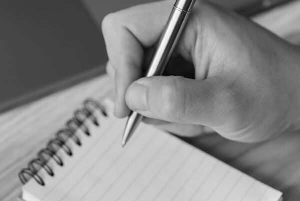 A hand writing with a pen on a blank notepad page