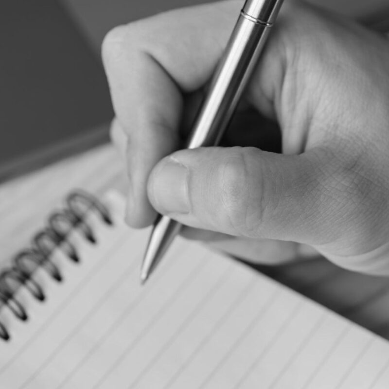 A hand writing with a pen on a blank notepad page