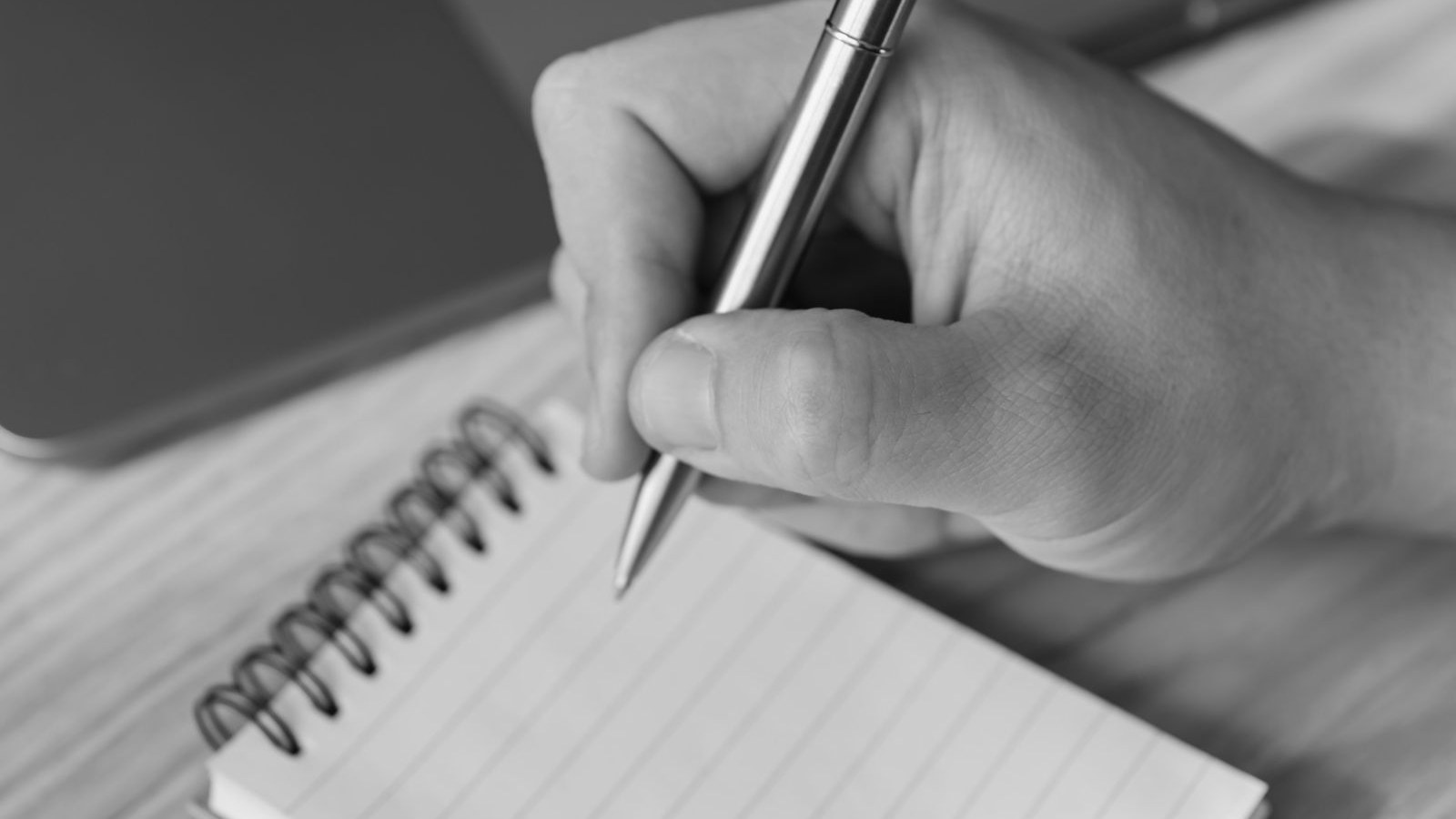 A hand writing with a pen on a blank notepad page