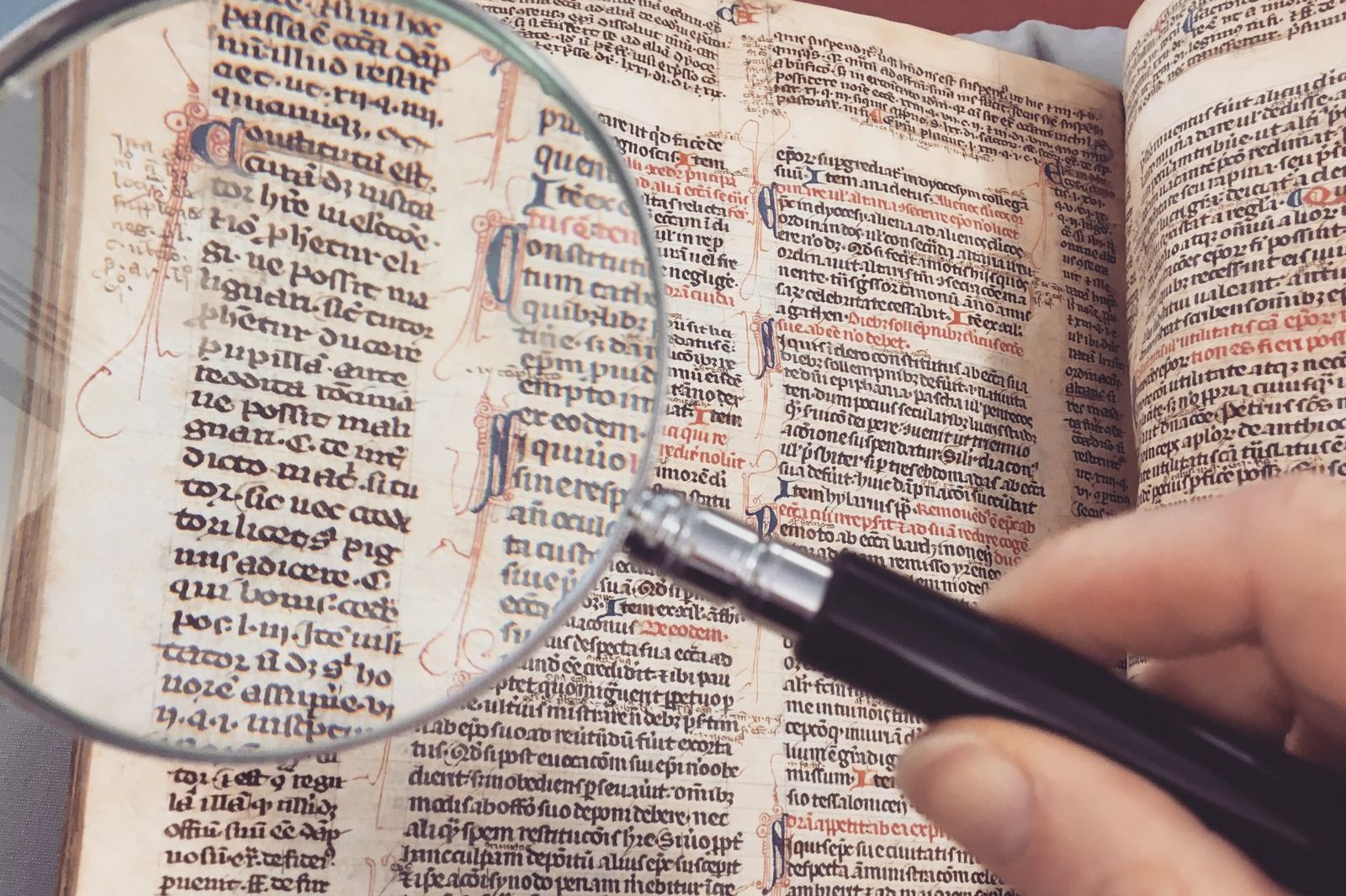 A hand holding a magnifying glass over the page of an old printed book