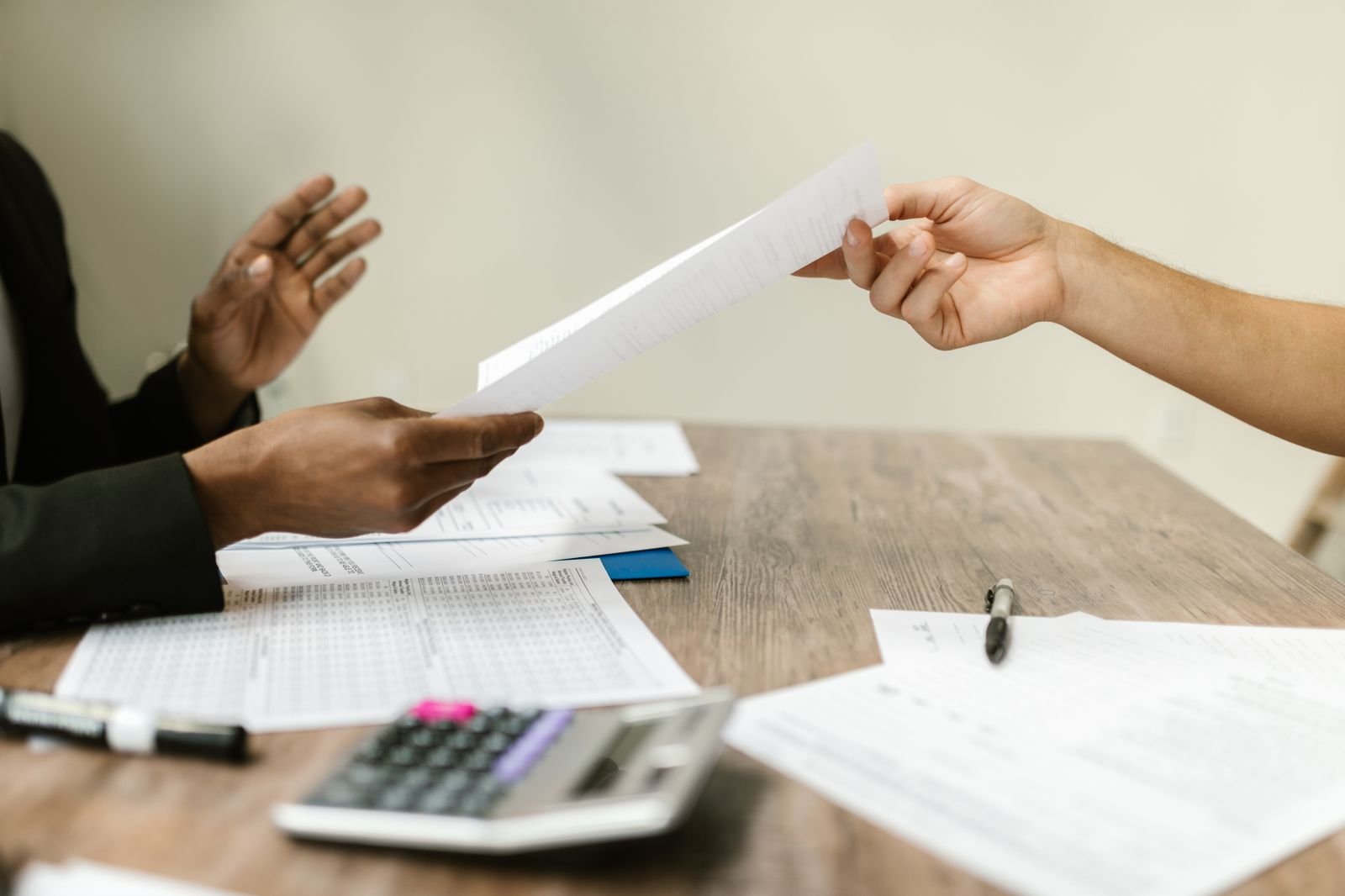 One person handing a sheet of paper across a desk to another person