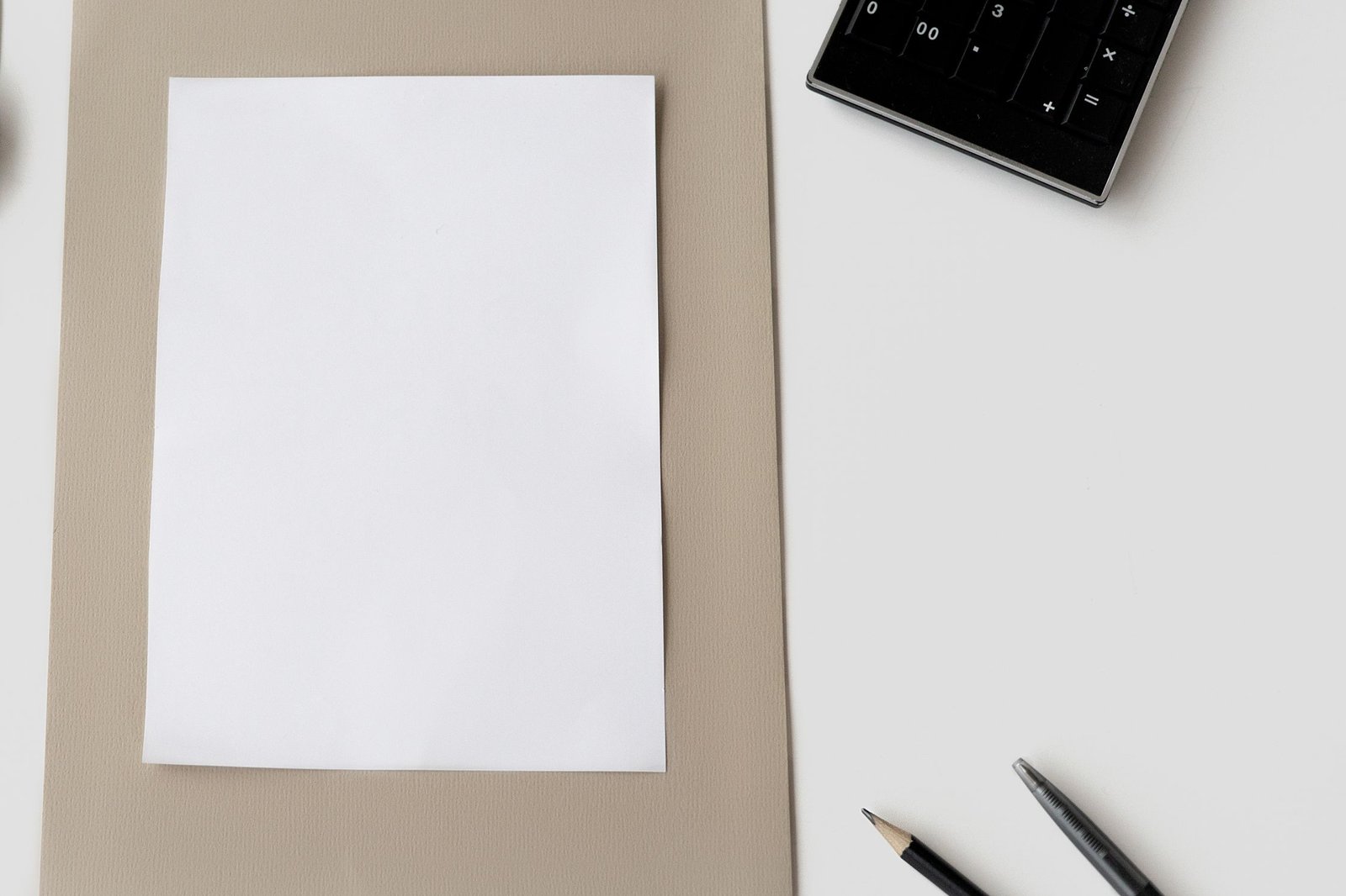 A blank sheet on a desk beside a calculator and pencils