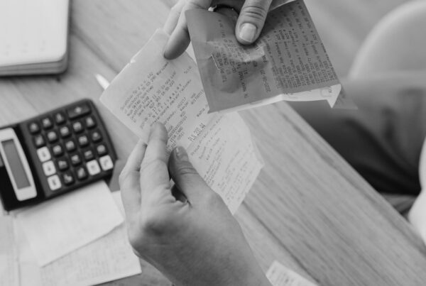 Hands holding paper receipts over a desk with a calculator and notes.
