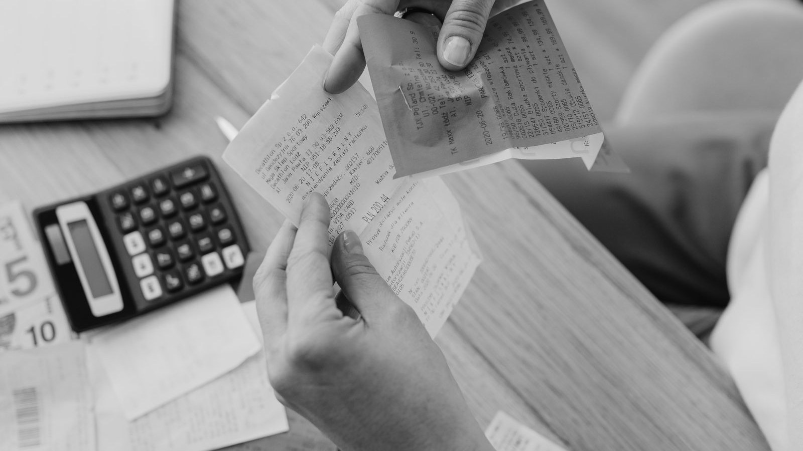 Hands holding paper receipts over a desk with a calculator and notes.