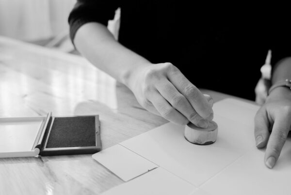 A hand pressing a stamp onto a blank sheet of paper, ink pad beside it
