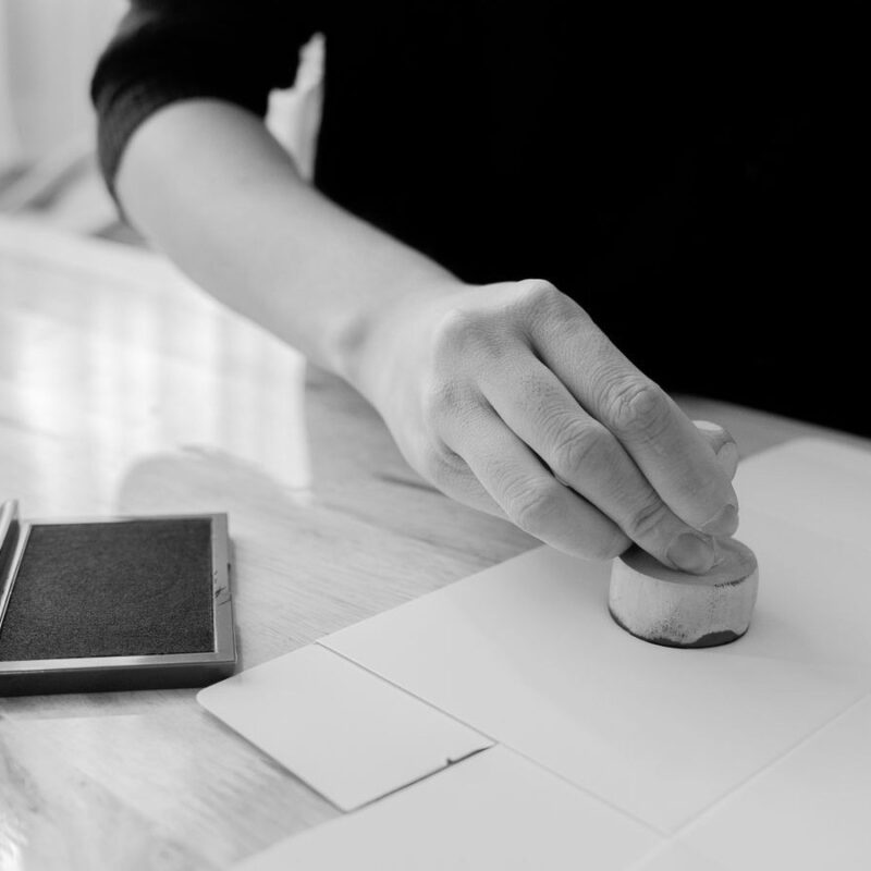 A hand pressing a stamp onto a blank sheet of paper, ink pad beside it